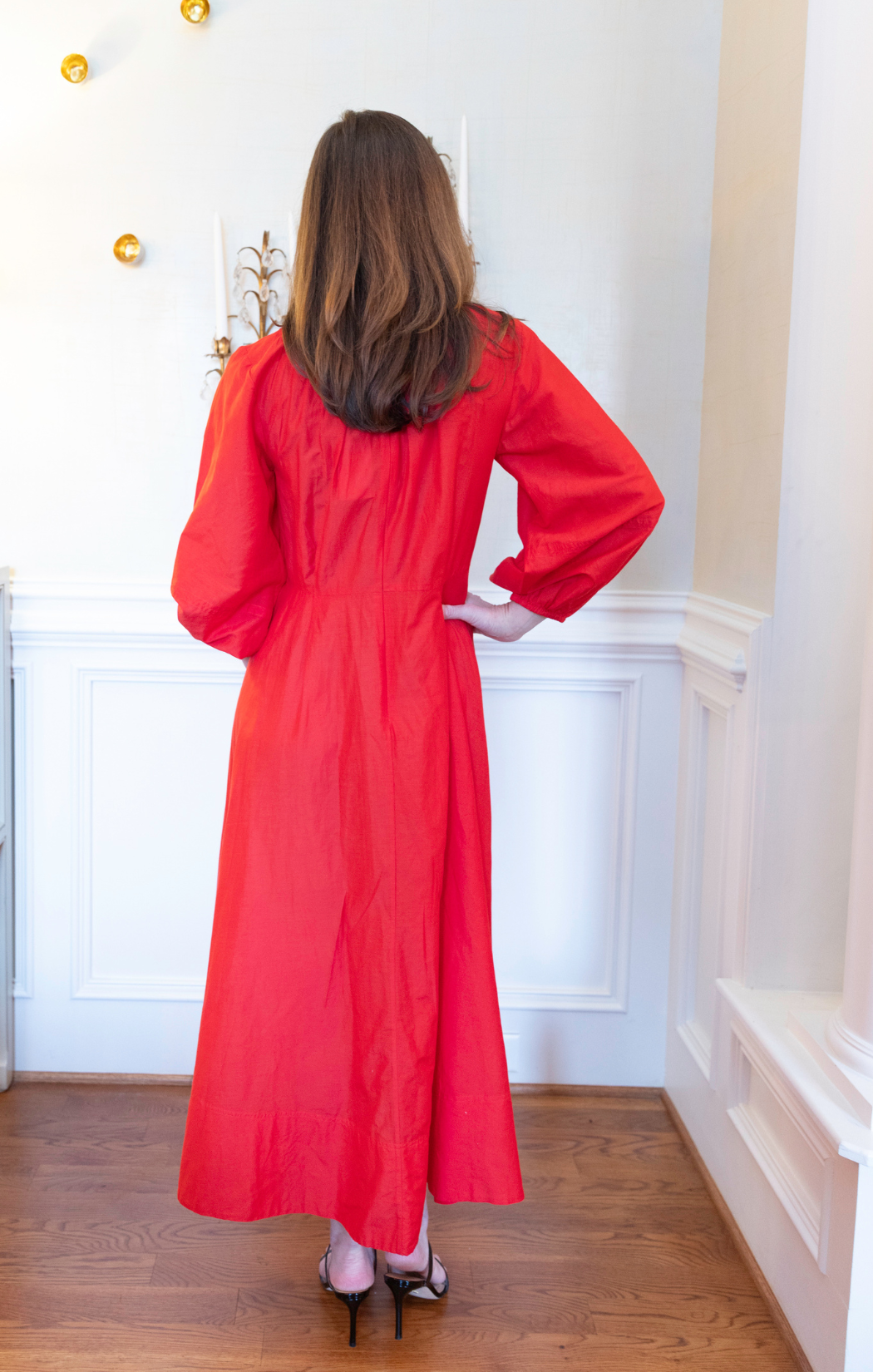 Person wearing a red dress standing in a room with white walls and wooden floor.