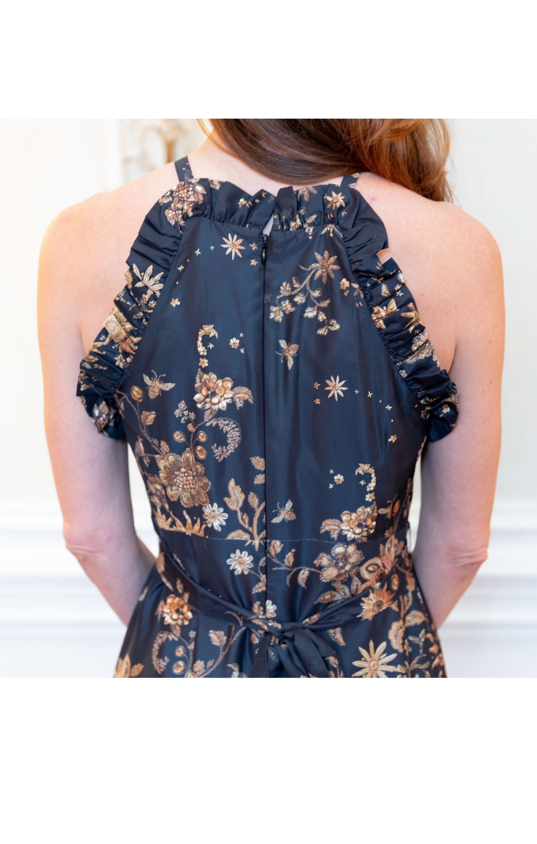 Black floral dress with ruffled straps worn by a person against a white background