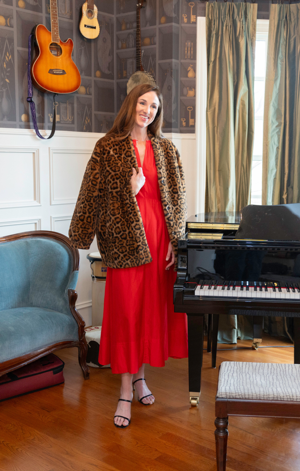 Woman in a red dress and leopard print coat standing in a room with a piano and guitars on the wall.