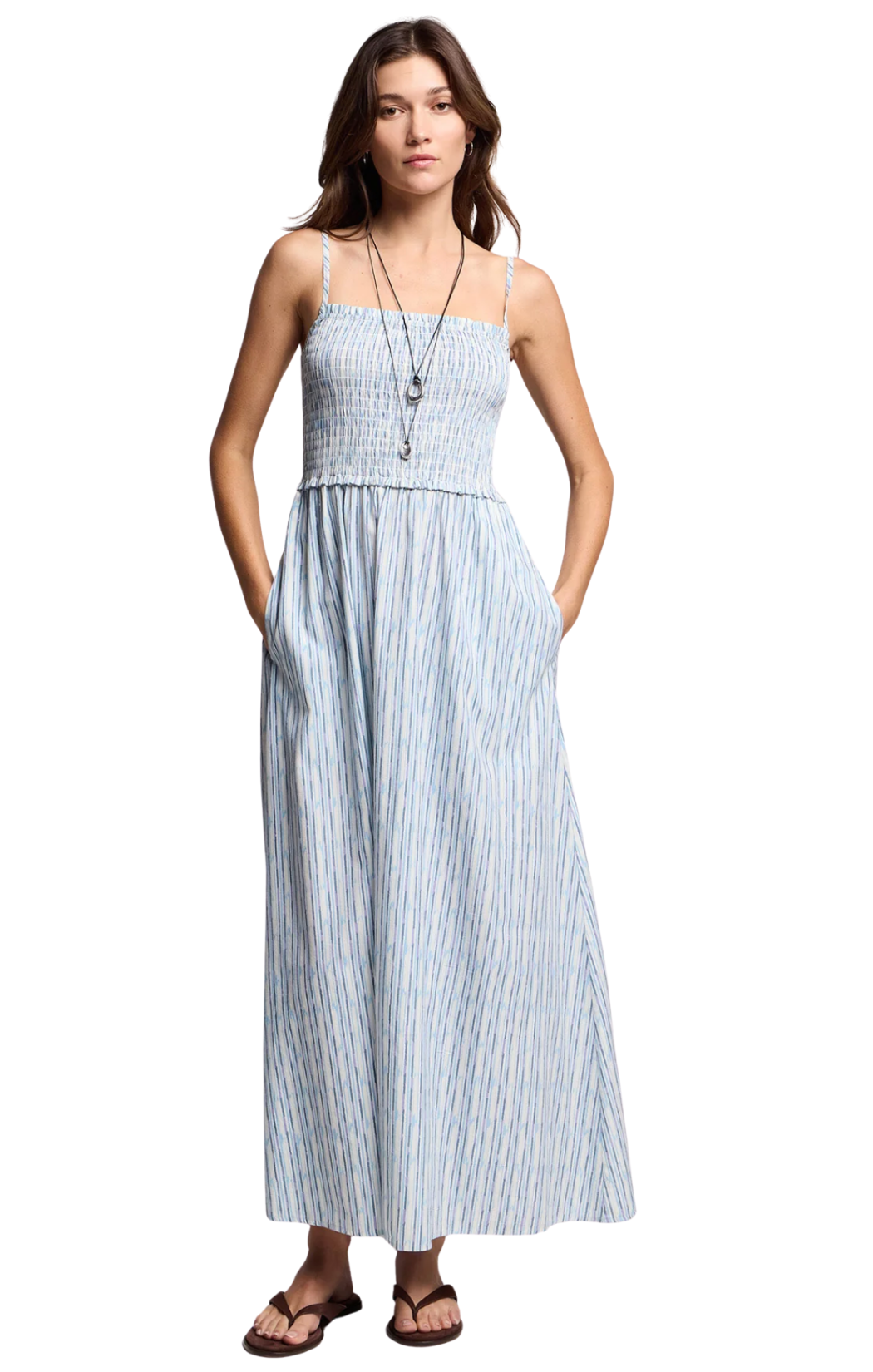 A blue and white striped maxi dress in a soft cotton-modal blend in a painterly watercolor stripe, with a smocked elastic bust, sleeveless silhouette, and adjustable straps