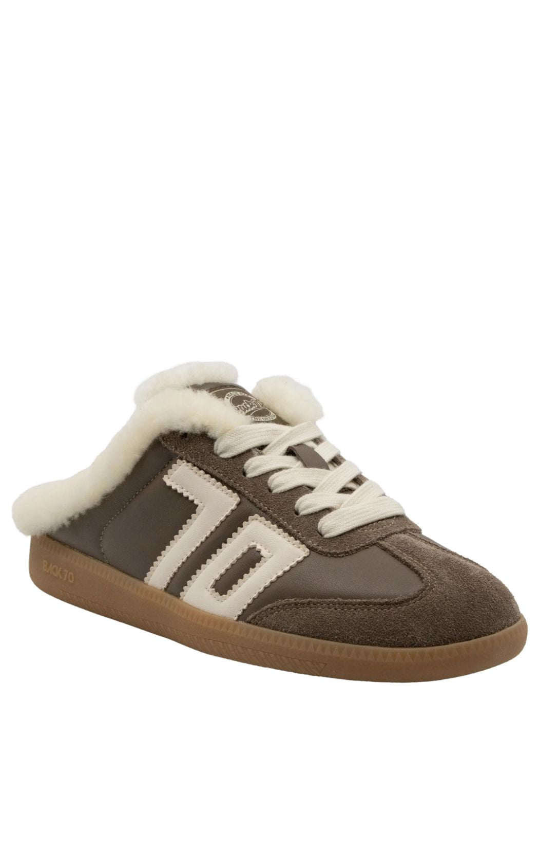 A slip-on mule sneaker in brown suede and faux leather with cream shearling lining, cream laces, and a tan rubber sole, shown on a plain white background.