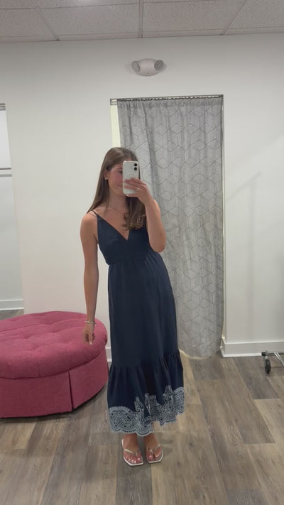 Woman facing forwarded in a navy dress with white embroidery at the bottom taking a selfie.